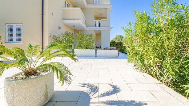 A modern multi-story building with a flat roof, a balcony, and a paved courtyard.