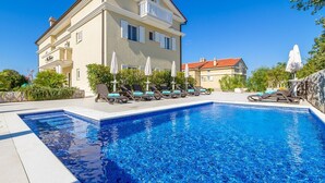 A two-story building with a swimming pool, lounge chairs, and umbrellas.