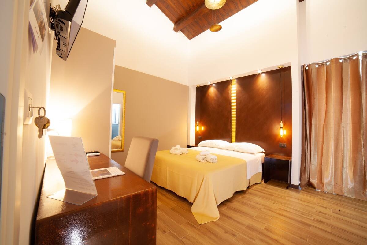 A hotel room with a wooden desk, two beds, a mirror, and a curtain.