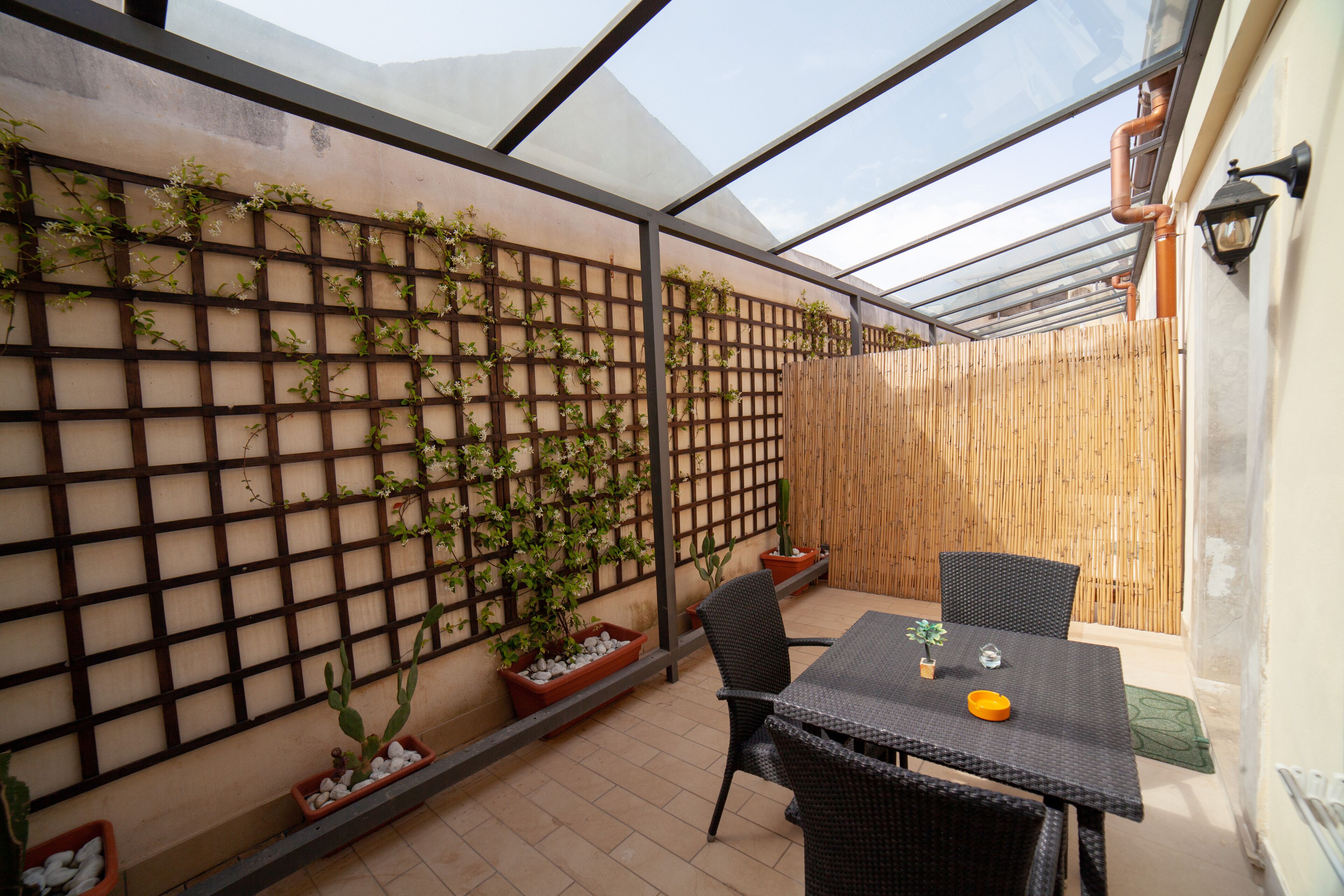 A covered patio area with a table and chairs, a wooden fence, and potted plants.