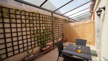 A covered patio area with a table and chairs, a wooden fence, and potted plants.
