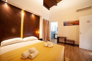 Habitación de hotel con cama, un banco, un cuadro y una puerta con número.