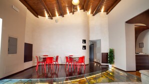 Un vaste espace intérieur doté d’un plancher en verre donnant sur un niveau inférieur, de chaises rouges disposées autour d’une table et d’un plafond en bois avec des luminaires encastrés.