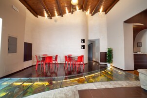 Amplio espacio interior con suelo de vidrio que da a un nivel inferior, sillas rojas alrededor de una mesa y techo de madera con iluminación empotrada.