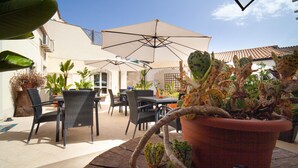 Une terrasse extérieure avec des tables et des chaises, entourée de plantes en pot et de parasols.