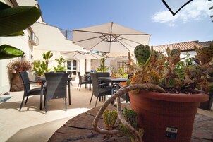 Un patio al aire libre con mesas y sillas, rodeado de plantas en macetas y sombrillas.