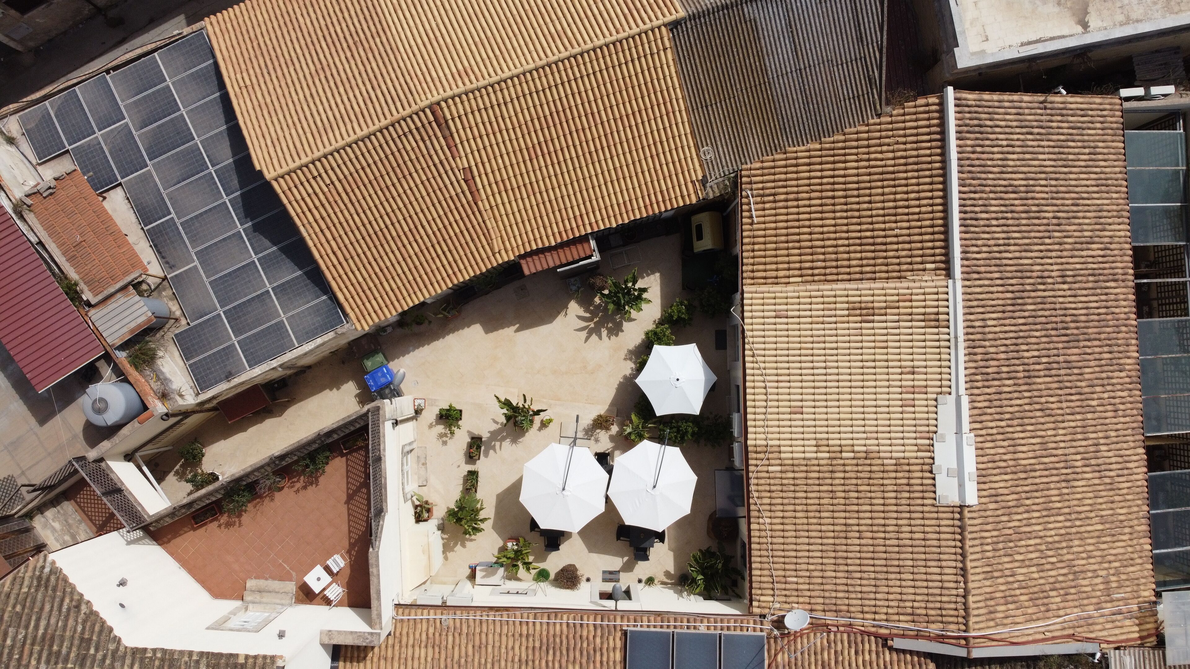 An aerial view of a rooftop with solar panels, a covered patio area with umbrellas, and a small seating area.
