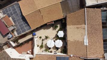 An aerial view of a rooftop with solar panels, a covered patio area with umbrellas, and a small seating area.