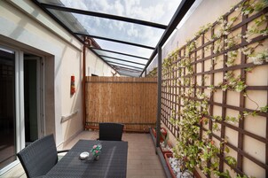 Un patio cubierto con mesa y sillas, cerca de madera y un muro cubierto de plantas trepadoras.