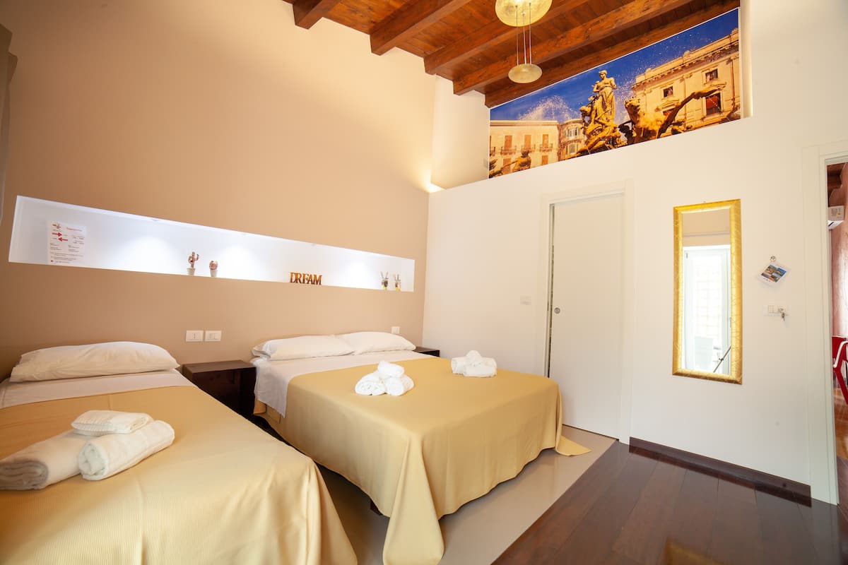 A hotel room with two beds, a large painting, a framed picture, and a door with a mirror.