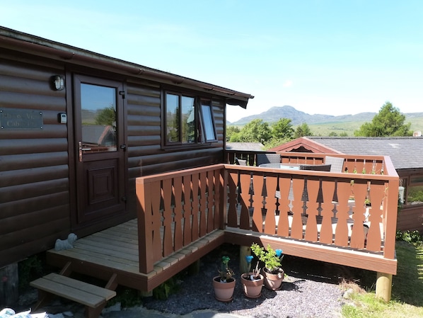 A wooden cabin with a balcony, a wooden deck, and potted plants.