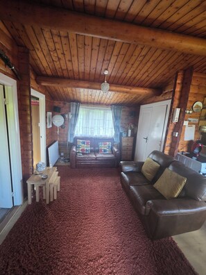 Ein gemütlicher Raum mit Holzbalkendecke, einem braunen Ledersofa, einem kleinen Holztisch und einem roten Teppich.