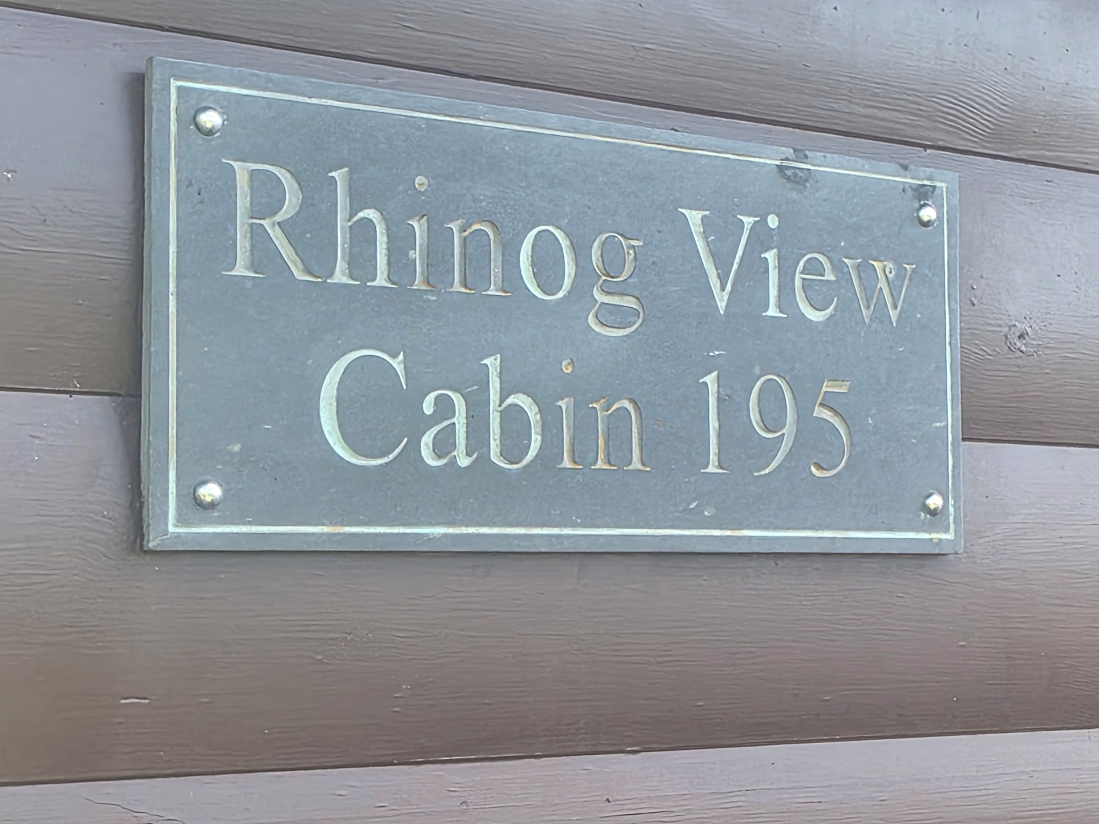 A metal sign with the text 'Rhino View Cabin 195' mounted on a wooden wall.