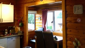 Interior acogedor de una cabaña con paredes de madera, un comedor, una cocina y una sala de estar con sofá y sillones.