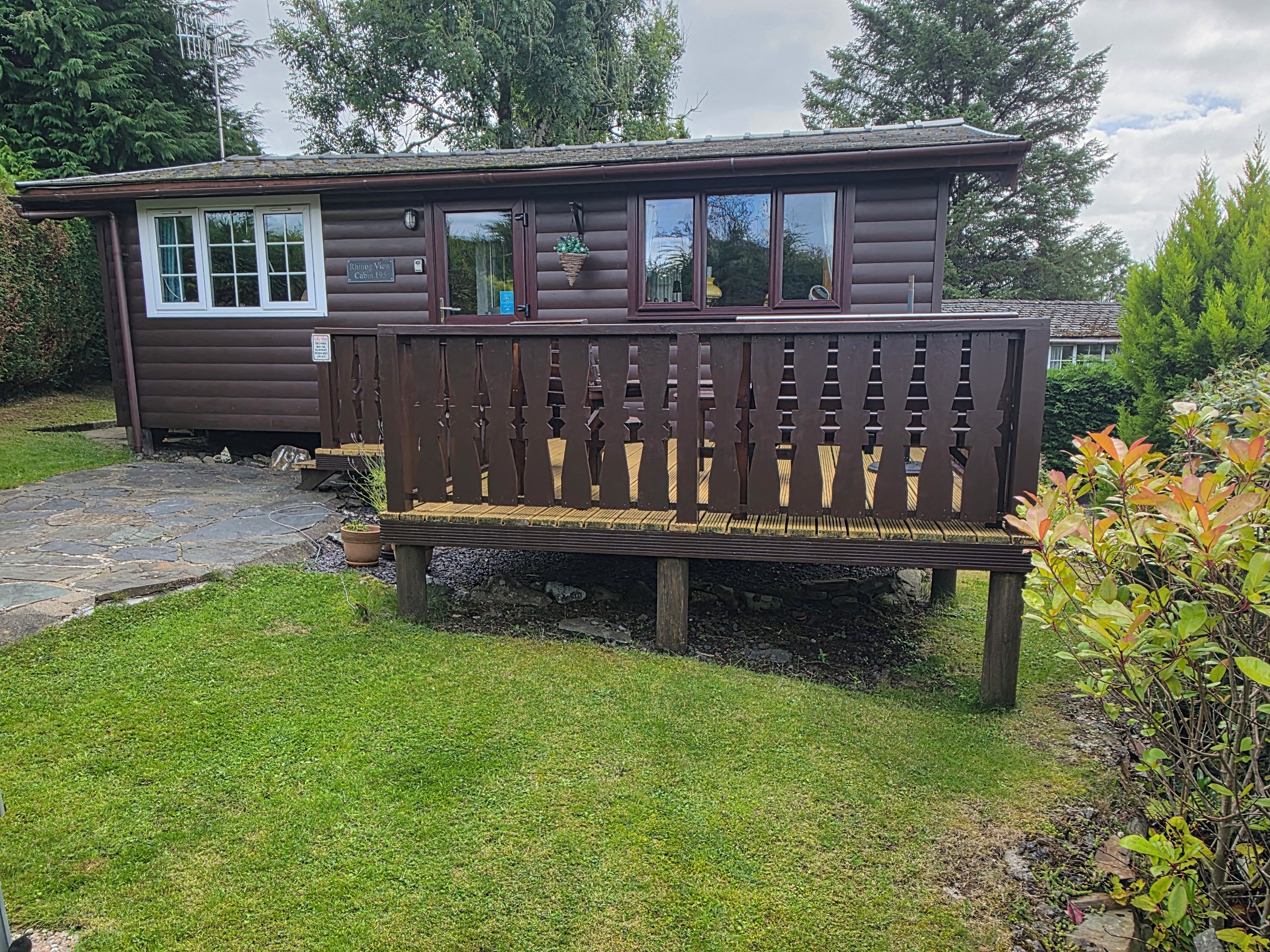 En stuga med en träveranda, en gång av sten och en gräsyta.