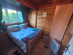 Ett sovrum i en stuga med träpanel, en säng, ett fönster med gardiner, ett element och en dörr.