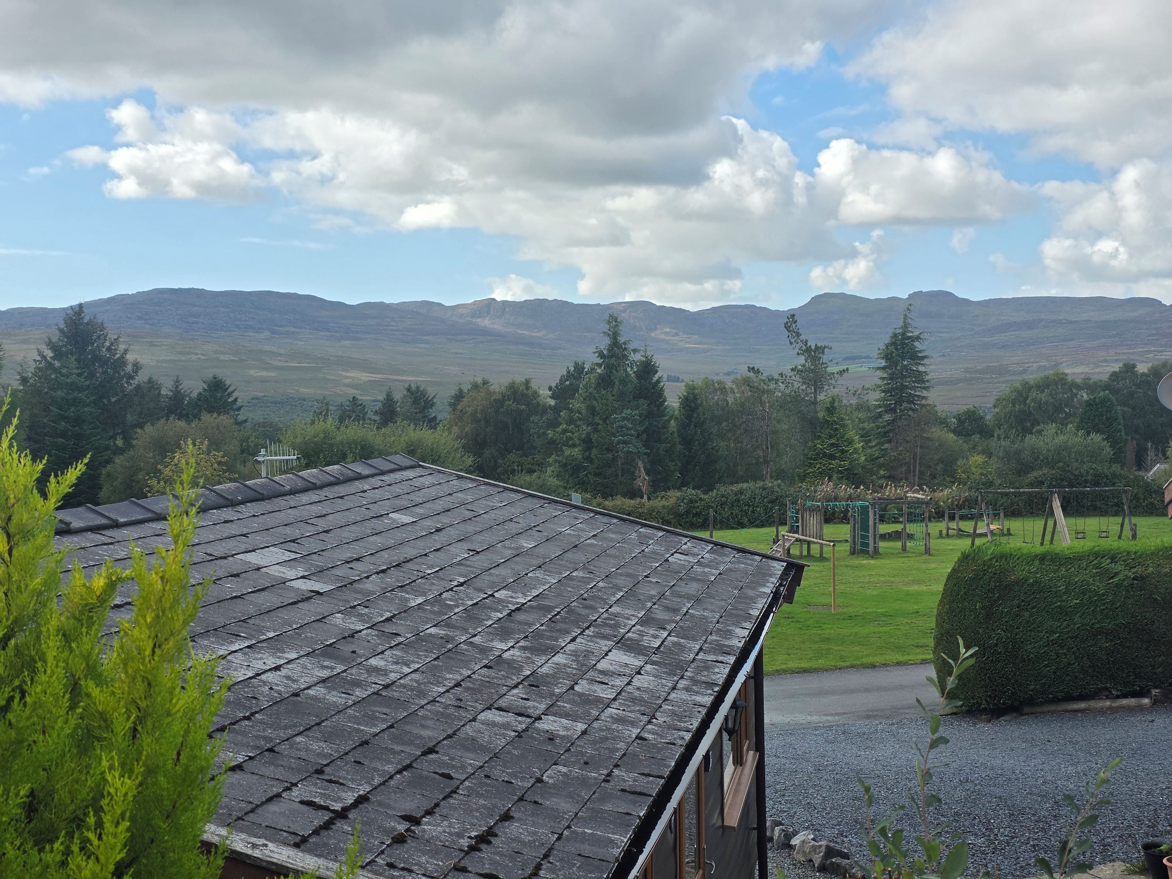 A building with a sloped roof, surrounded by a well-maintained garden with a swing set and a neatly trimmed hedge.