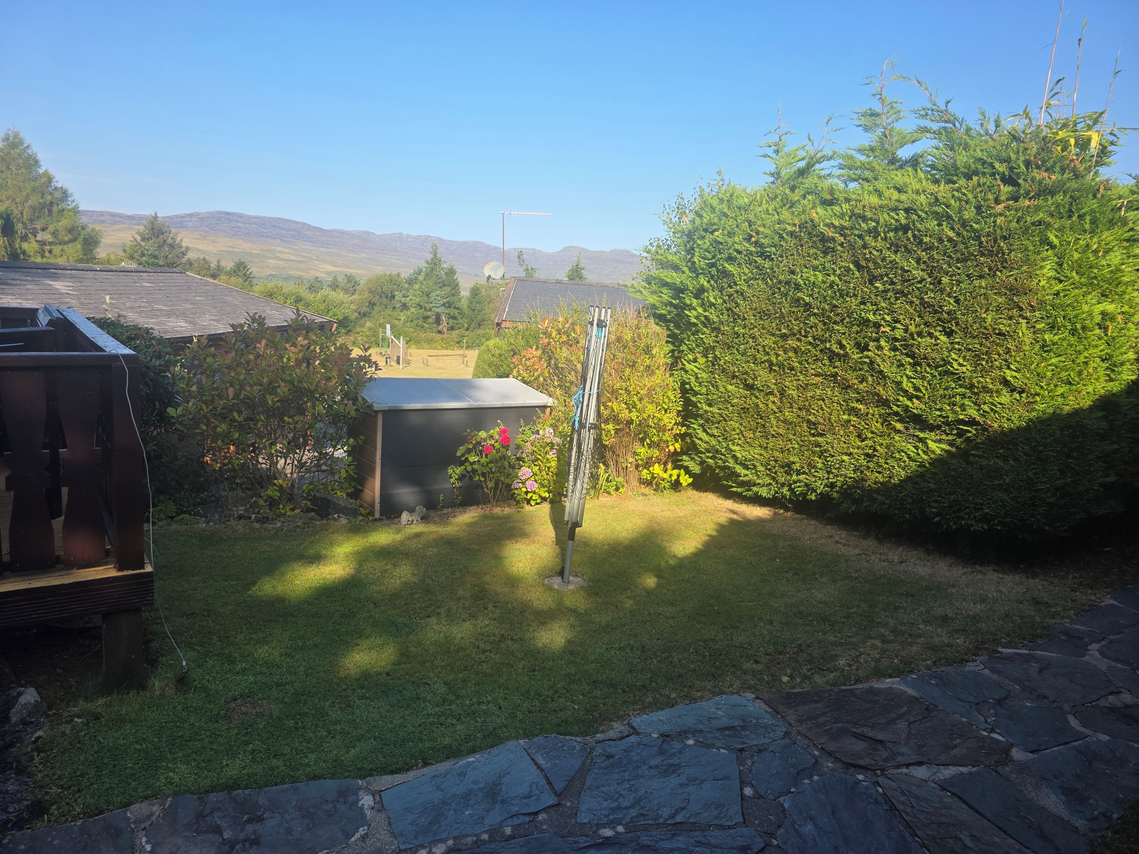 A garden with a wooden deck, a shed, and a stone pathway.