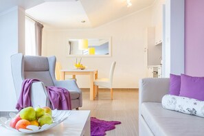 Un salon moderne avec un canapé gris, une table à manger avec des chaises et un panier de fruits posé sur une table blanche.