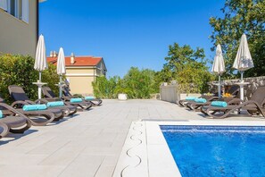 Ein Poolbereich auf dem Dach mit Liegestühlen und Sonnenschirmen, ein klarer, blauer Himmel und ein Gebäude im Hintergrund.