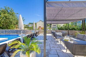 Un espace aménagé au bord de la piscine, avec des chaises longues, un coin salon abrité et un mur en pierre.