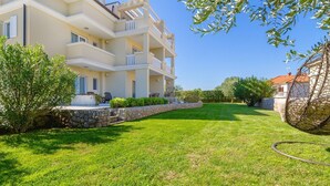 A multi-story building with balconies, a stone retaining wall, and a well-maintained lawn.