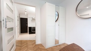 A room with a herringbone floor, a wooden bench, a white wardrobe with a mirror, and a door leading to a kitchen area. - Warsaw Concierge Square Grzybowski (Warsaw)