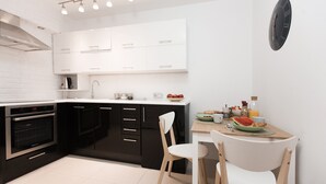 A modern kitchen with black and white cabinetry, a built-in oven, and a dining area with two chairs and a table set for breakfast. - Warsaw Concierge Square Grzybowski (Warsaw)