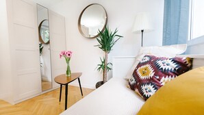 A bedroom with a bed, a small table with flowers, a mirror, and a potted plant. - Warsaw Concierge Square Grzybowski (Warsaw)