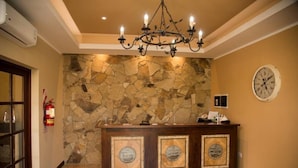 A reception area with a stone wall, a wooden reception desk, a chandelier, a clock, and a fire extinguisher.