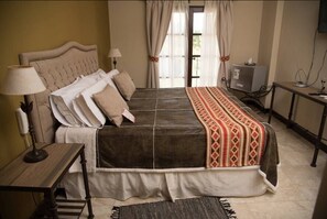 Ein Schlafzimmer mit einem großen Bett, einem Schreibtisch, einem Sessel, einer Lampe und einem Fernseher.