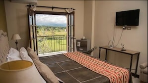 A bedroom with a bed, a desk, a TV, and a balcony with a view.