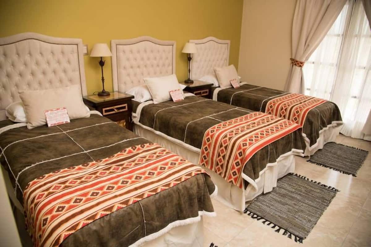 Habitación de hotel con tres camas, cada una con cabecero y mesitas de noche.