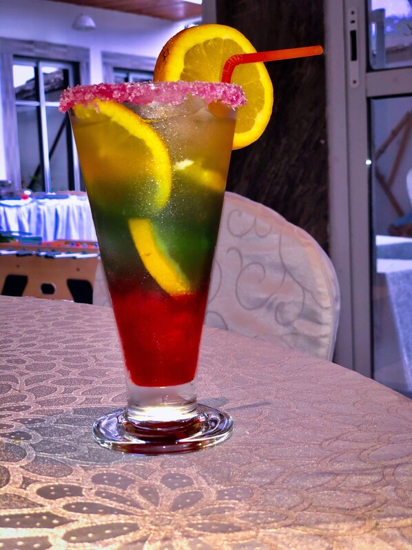 A glass with a layered drink, garnished with a slice of orange and a pink rim. - Residence Hoteliere Flana B (Libreville)
