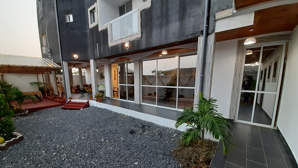 A building with a covered patio area, a gravel courtyard, and a tiled walkway. - Residence Hoteliere Flana B (Libreville)
