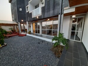 A building with a covered patio area, a gravel courtyard, and a tiled walkway. - Residence Hoteliere Flana B (Libreville)