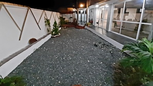 A courtyard with a gravel ground, potted plants, and a white wall with geometric patterns. - Residence Hoteliere Flana B (Libreville)