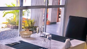 A table set with cutlery, a glass, and a bowl, with a view of a building and plants outside. - Residence Hoteliere Flana B (Libreville)