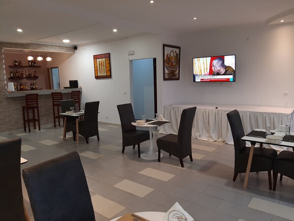 A restaurant with a bar area, multiple tables, chairs, and a television displaying a news channel. - Residence Hoteliere Flana B (Libreville)