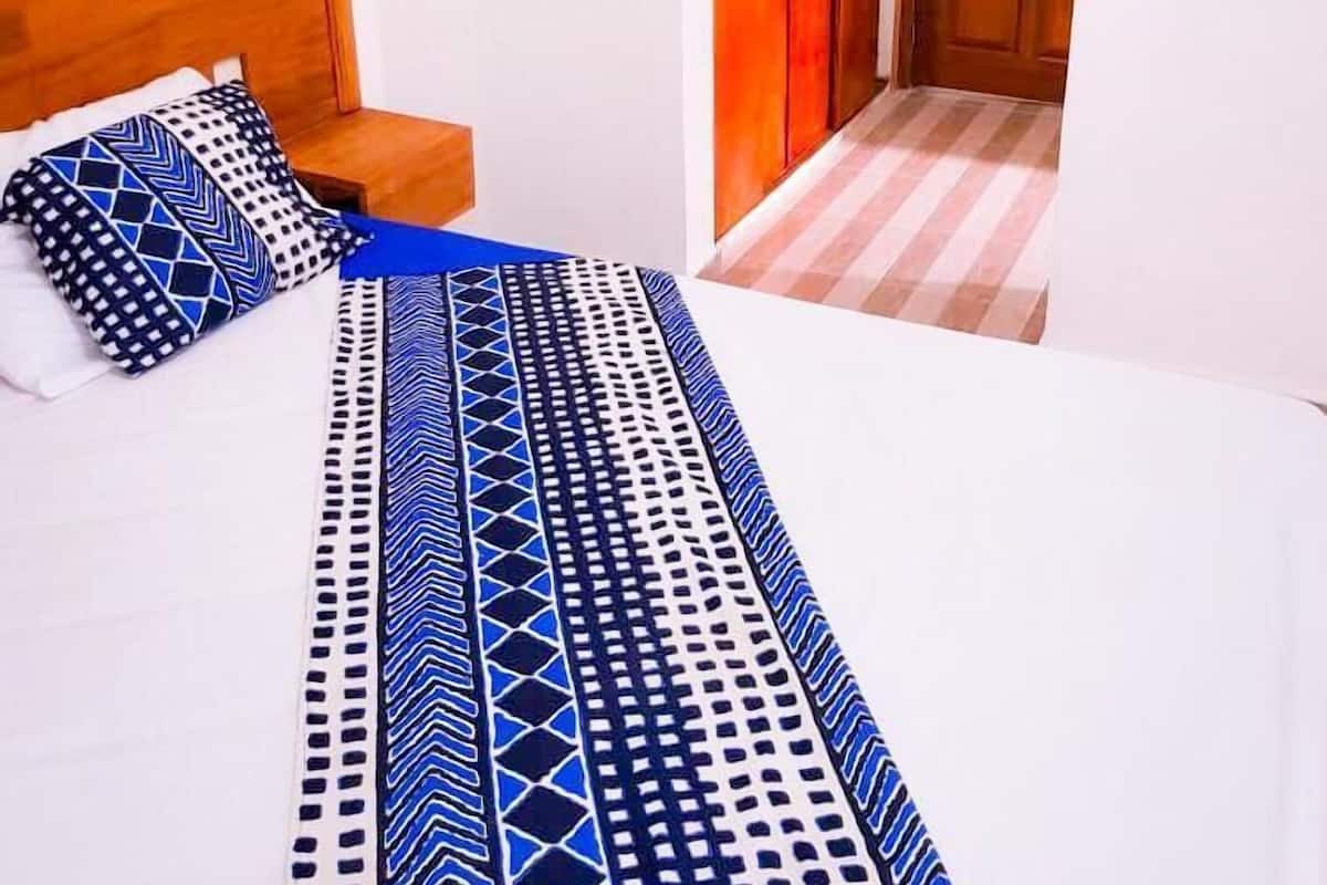 A bedroom with a wooden headboard, a bed with a patterned bedspread, a small bedside table, and a wardrobe.