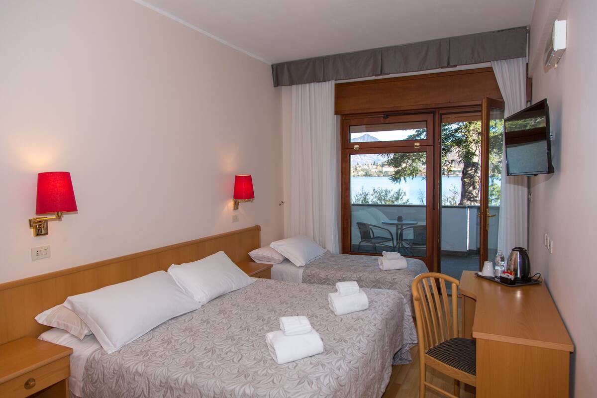 A hotel room with two beds, a desk, a chair, a TV, and a balcony with a view.