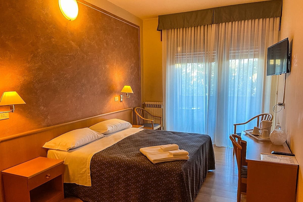 A hotel room with a bed, bedside lamps, a desk, and a television.