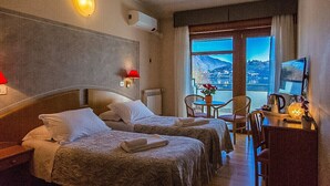 A hotel room with two beds, a desk with a computer, a chair, and a view of a mountainous landscape.