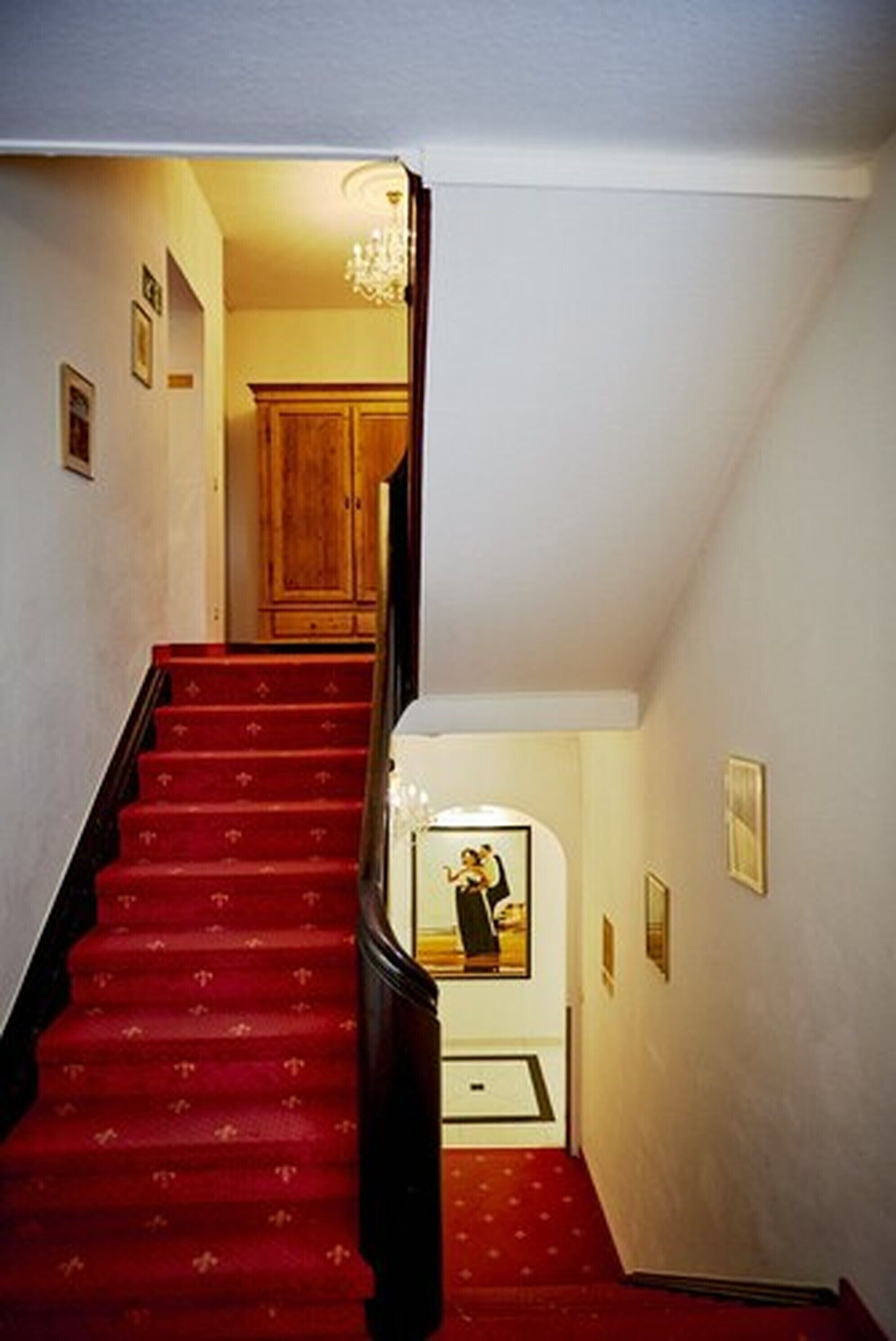 Un escalier dont les marches sont recouvertes d’une moquette rouge, menant à une porte en bois située en haut.
