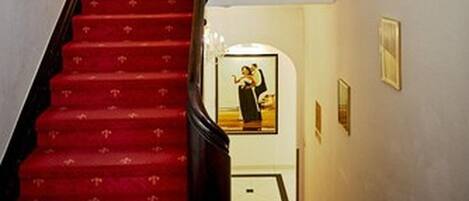 Una escalera con peldaños cubiertos de alfombra roja que conducen a una puerta de madera en la parte superior.