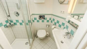 A bathroom with a glass shower enclosure, a toilet, and a sink.