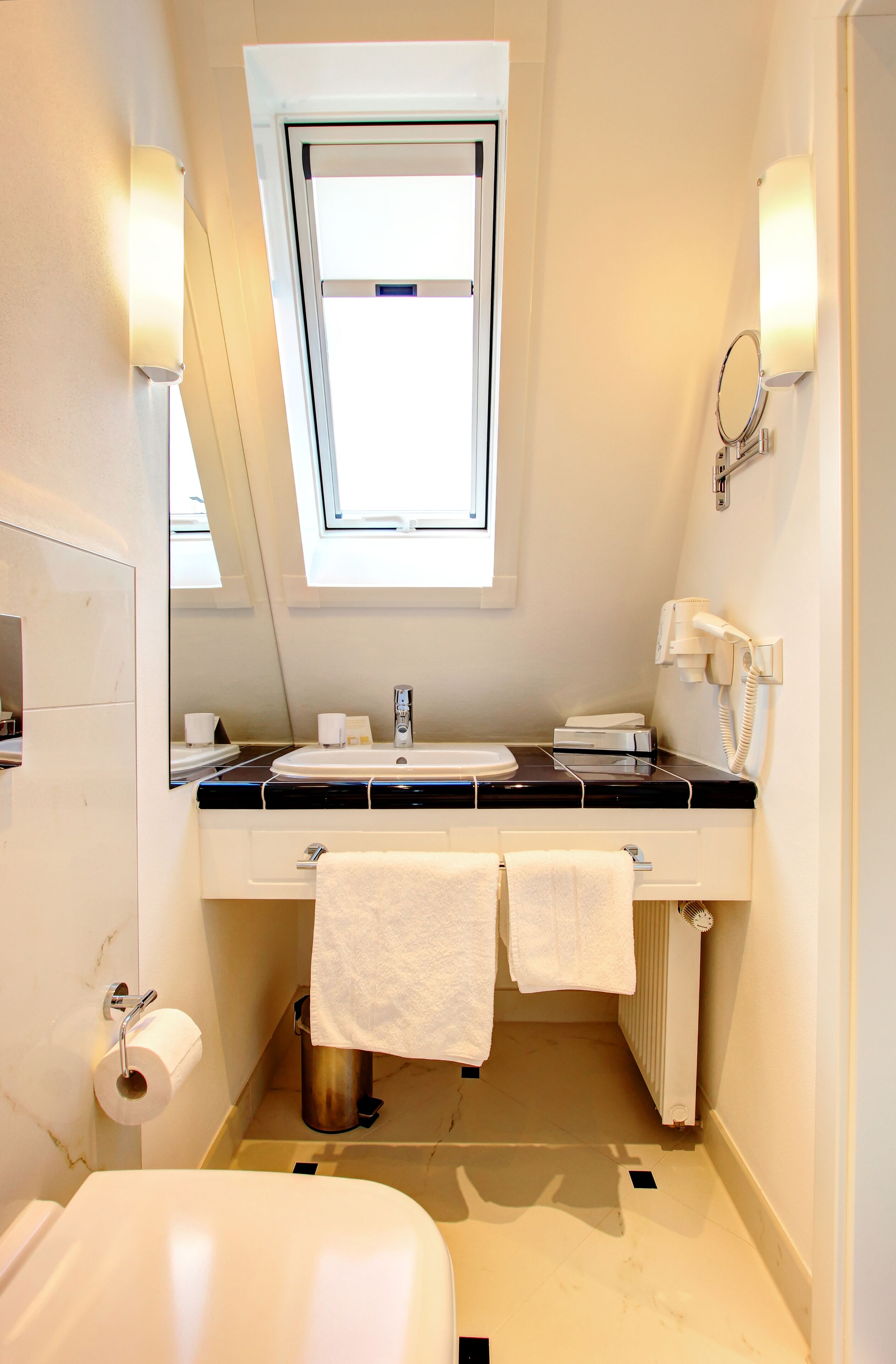 Une petite salle de bain moderne avec un puits de lumière, un lavabo, des toilettes et un porte-serviettes.