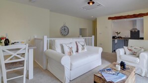A cozy living room with a white sofa, a dining table, and a kitchen area in the background. - Seaview 1 Bed Apartment Sleeps 4 - Balcony - Tv (Lynmouth)