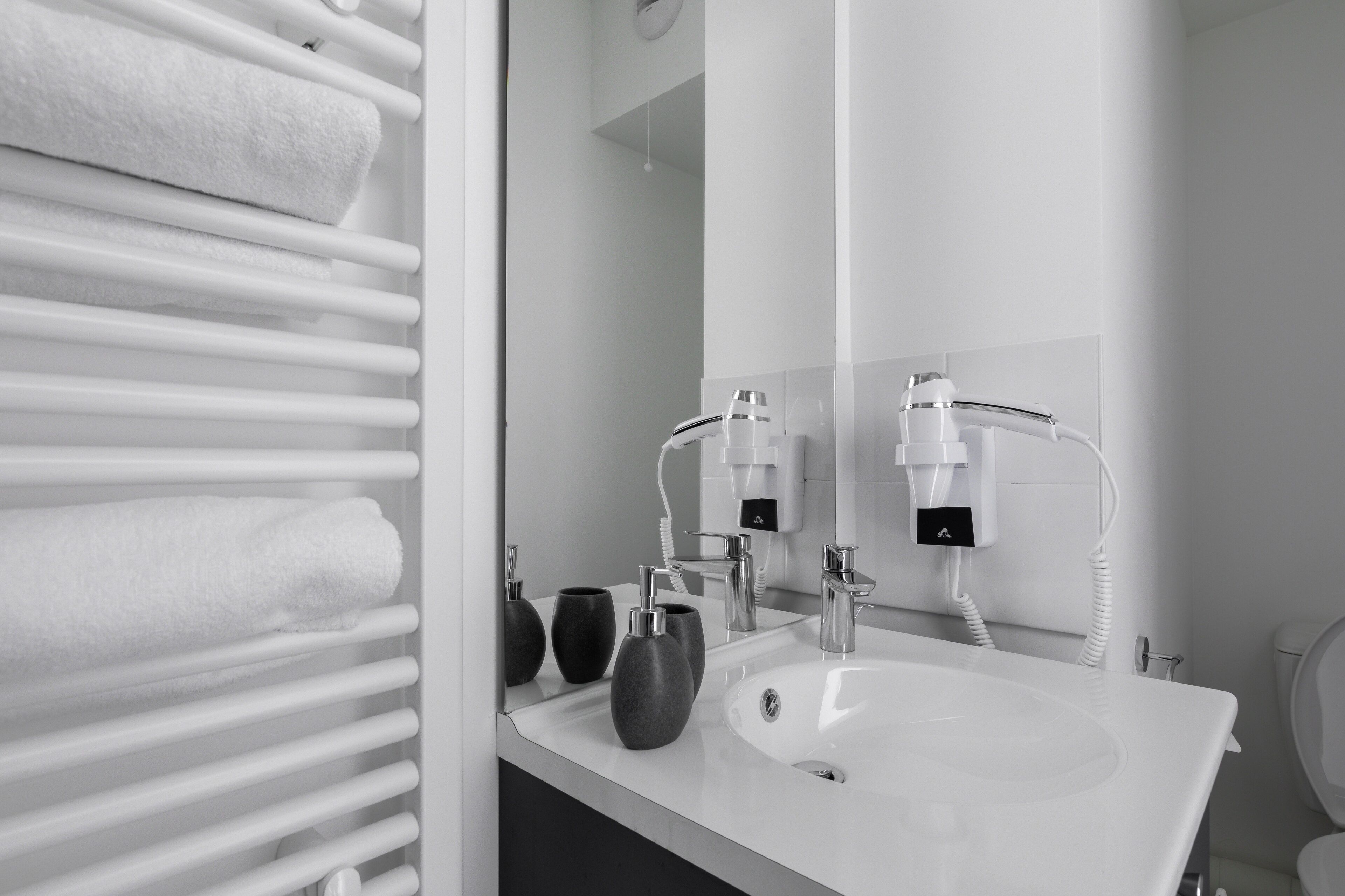 Une salle de bain moderne avec un lavabo blanc, deux robinets et un porte-serviettes sur lequel sont pliées des serviettes.