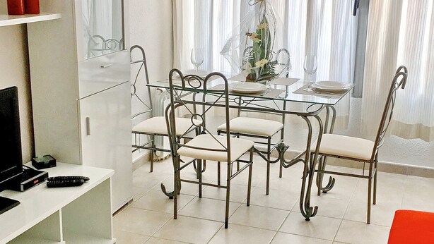 A dining area with a glass table and metal chairs, a white cabinet with a TV, and a red chair.